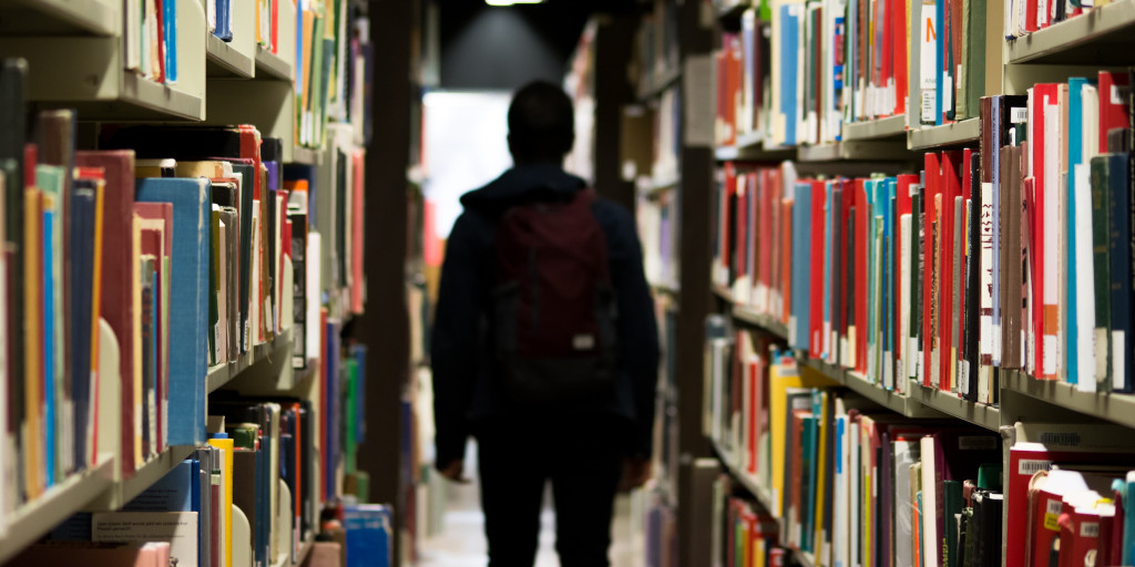 Fate_Photo by Redd on Unsplash. Shows a silhouetted figure in a library.